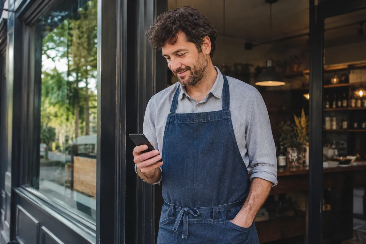 Independent shop owner checking their phone in the doorway of their business